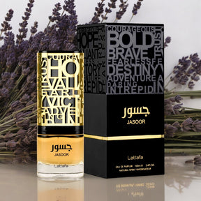 A perfume bottle labeled "Jasoor EDP" from the brand Lattafa. The clear 3.4 oz (100 ml) bottle with a gold cap and intricate geometric designs houses a sophisticated scent. The packaging is black with bold gold text and features words like "Courageous" and "Bold." Lavender sprigs in the background hint at this men's fragrance's spicy and woody notes.