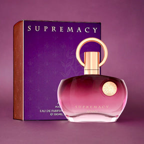 A bottle of Afnan's "Supremacy Purple EDP Perfume for Women 3.4 oz/100 ml" is displayed beside its coordinating purple box adorned with gold accents. The perfume bottle boasts a curvy, translucent design with a gold circular cap and a decorative gold emblem, encapsulating elegance and charm. The box features the same "Supremacy" branding.