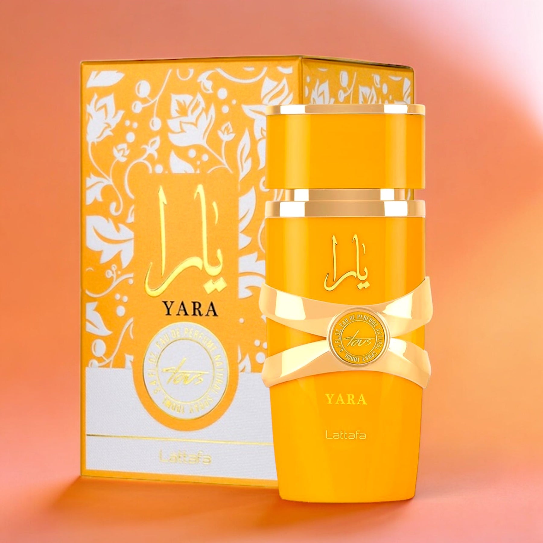 The "Yara Tous EDP Perfume for Women 3.4 oz/100 ml" by Lattafa is showcased in front of its matching box. The brightly colored yellow bottle is labeled with "Yara," while the box features decorative white floral patterns on a yellow background, exuding tropical elegance. The bottle itself is adorned with gold accents and a ribbon motif, epitomizing luxury fragrance.